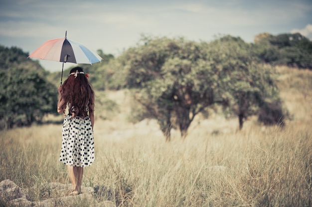 Ein Zigeunermädchen, das Regenschirm und Stand alleine in der Wiese hält