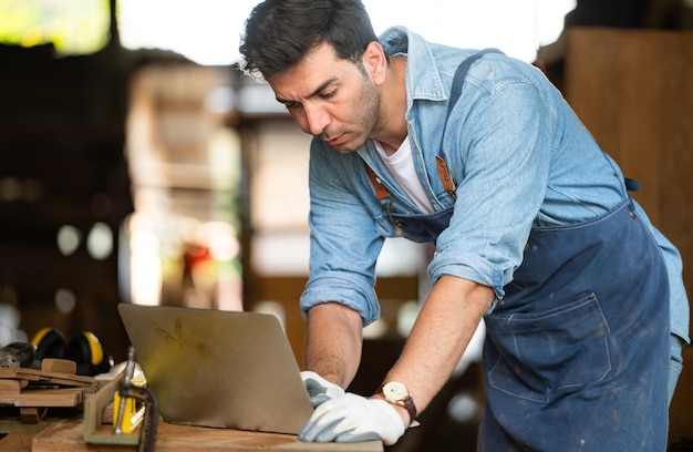 Ein Zimmermann arbeitet in seiner Werkstatt an einem Laptop in einer Holzbearbeitungsfabrik