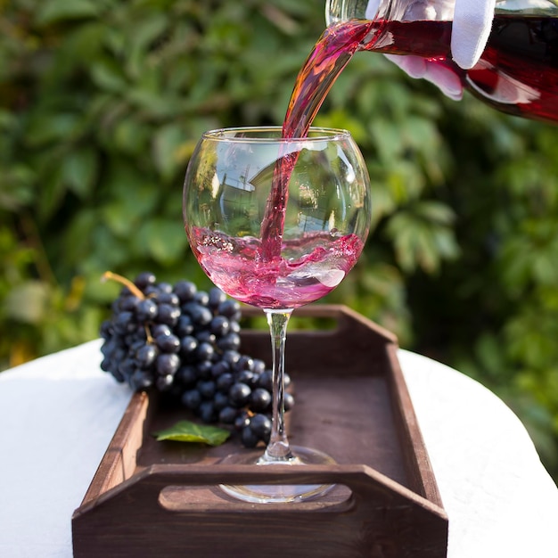 Ein zur Verkostung vorbereitetes Glas Rotwein steht auf einem Tisch mit weißer Tischdecke im Freien im Sonnenlicht