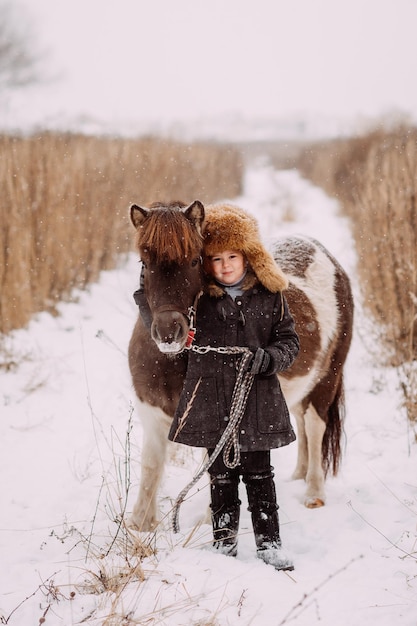 Ein zweifarbiges Pony und ein Kind laufen durch ein Schneefeld 3090