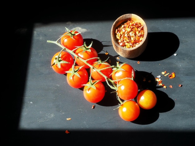 Ein Zweig Kirschtomaten und eine Holzschale mit Gewürzen auf schwarzem Hintergrund