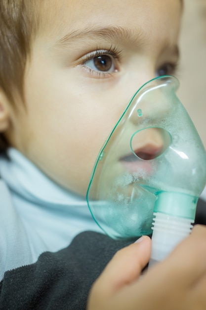 Einatmungstherapie des schönen kranken Jungen durch die Maske des Inhalators.