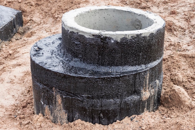 Einbau eines Stahlbetonbrunnens zur Wasserversorgung und Kanalisation auf der Baustelle Brunnenringe mit gusseiserner Luke und Bauwerkzeug