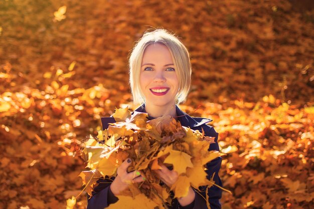 Eine 3040 Jahre alte Frau hält im Herbst im Park vor dem Hintergrund goldener Laubblätter gelbe Blätter in den Händen