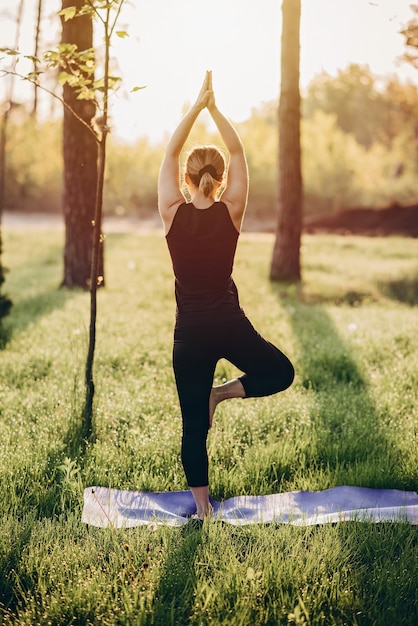 Eine 36-jährige Frau praktiziert Yoga an einem frühen sonnigen Morgen im Wald zwischen den Bäumen. Weicher selektiver Fokus.