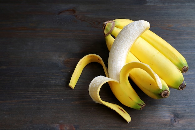Eine abgezogene Banane auf einem Bündel Bananen lokalisiert auf dunkelbraunem Holztisch