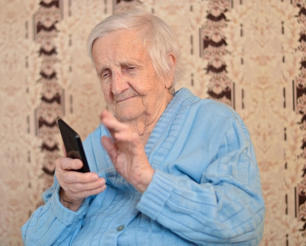 Foto eine ältere 90-jährige frau mit brille und blauer jacke lächelt mit einem smartphone