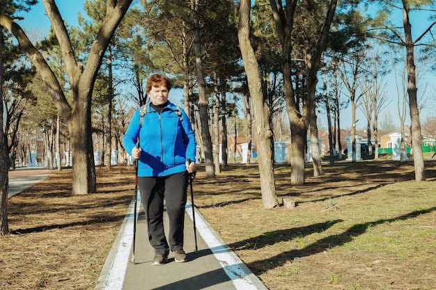 eine ältere aktive Frau geht im Park auf skandinavischen Stöcken Gesunder Lebensstil erwachsener Frauen