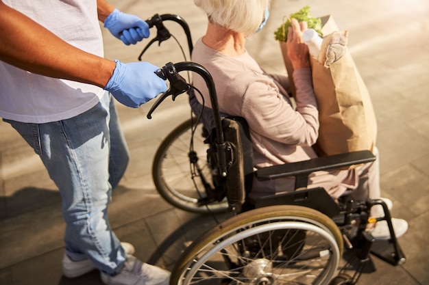 eine ältere behinderte Person mit einer Papiertüte in den Händen auf dem Weg vom Einkaufszentrum