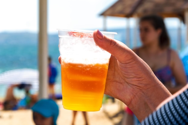 Eine ältere Frau hält am Strand ein Glas Bier in der Hand