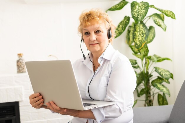 Eine ältere Frau hält einen Laptop und ruft an. Oma genießt die Unterstützung vor Ort.