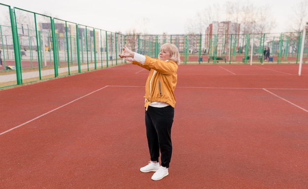 Eine ältere Frau in einer gelben Jacke macht Sportübungen auf einem roten Laufband. Das Stadion ist ein gesunder Lebensstil. Rentner und Sport. aktive alte Frau