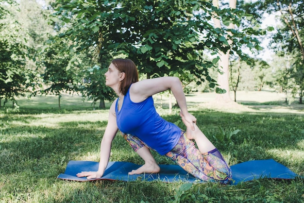 Eine ältere Frau macht Yoga im Park auf einer Matte Führt komplexe Asana-Übungen durch, führt zu einem gesunden Leben
