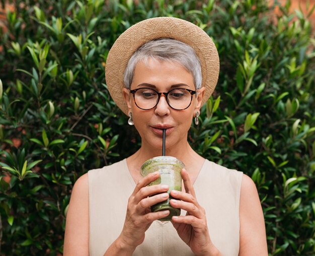 Eine ältere Frau mit kurzen Haaren trinkt einen Smoothie, eine ältere Frau genießt einen Cocktail im Freien