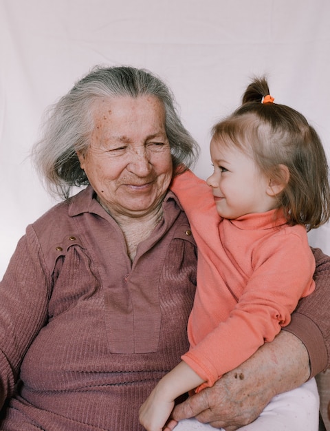 Eine ältere Großmutter hält ein schönes kleines Mädchen in ihren faltigen Armen. Familiengeneration. Jugend und Alter. ältere Menschen