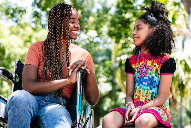 Eine Afroamerikanerin im Rollstuhl, die einen Tag im Park genießt und Spaß mit ihrer Tochter hat