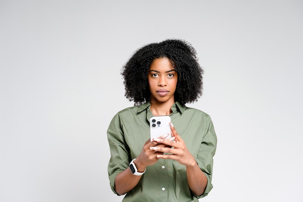 Eine afroamerikanische Frau steht ruhig und hält ein Smartphone in beiden Händen mit einem ernsten Gesichtsausdruck