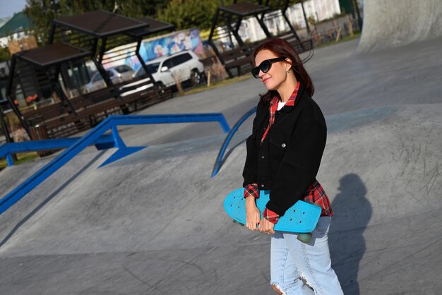 Eine aktive Frau mittleren Alters fährt auf einer leeren Straße oder Autobahn mit einem Skateboard, eine gewöhnliche Stadtfrau entspannt sich nach der Arbeit mit einem Skateboard, das Konzept eines modernen Lebensstils.