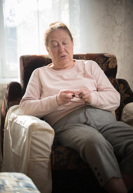 Eine alte Frau im Pullover sitzt im Sessel und strickt