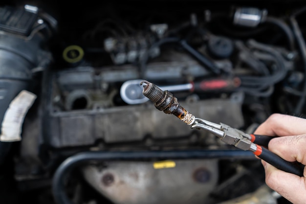 Eine alte Zündkerze in den Händen eines Meisters vor dem Hintergrund des Motors