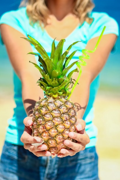 Eine Ananas in den Händen eines Mannes am Meer in der Natur auf einem Reisehintergrund