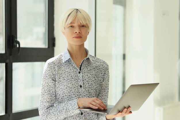 Eine Arbeiterin steht im Büro und hält einen Arbeitslaptop auf der Handfläche