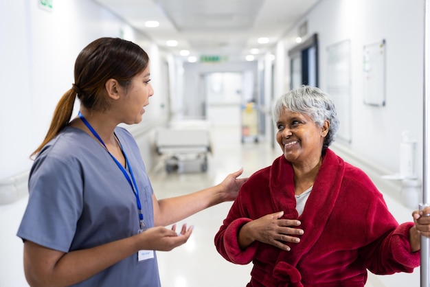 Eine asiatische Ärztin spricht mit einer lächelnden, vielfältigen älteren Patientin im Krankenhausflur. Krankenhaus, medizinische und Gesundheitsdienstleistungen.