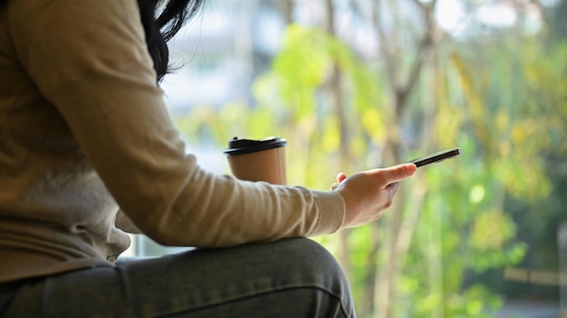 Eine asiatische Frau entspannt sich im Café mit ihrem Smartphone und nippt an Kaffee