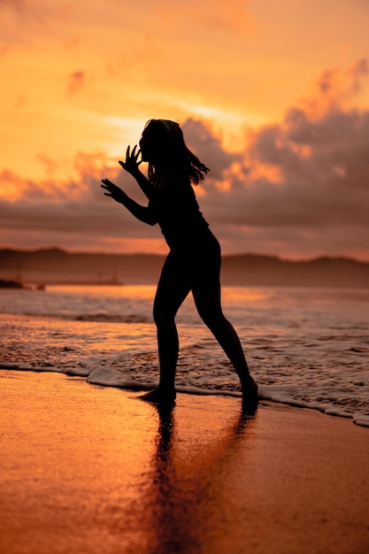 Eine asiatische Frau in Form einer Silhouette, die am Strand sehr agil Ballettbewegungen ausführt