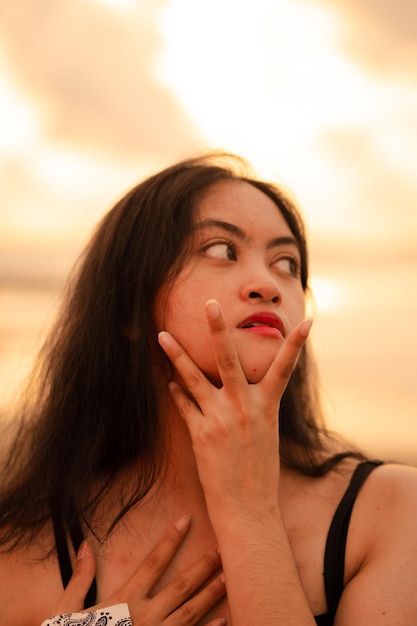 Eine asiatische Frau mit langen schwarzen Haaren posiert mit ihren Händen und genießt dabei den Blick auf den Strand