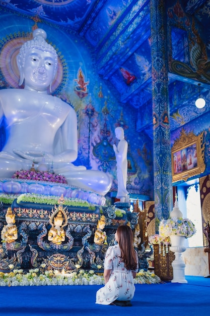 Eine asiatische Frau sitzt vor der Buddha-Statue im Wat Rong Suea Ten, dem blauen Tempel in Chiang Rai, Thailand?