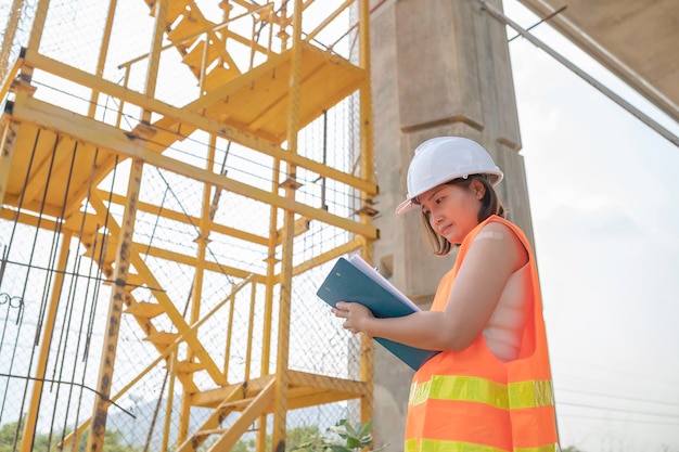 Eine asiatische Ingenieurin arbeitet auf einer AutobahnbrückenbaustelleBauarbeiter bei der Kontrolle der Arbeiten am Kreuzungsbau