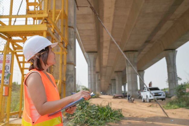 Eine asiatische Ingenieurin arbeitet auf einer AutobahnbrückenbaustelleBauarbeiter bei der Kontrolle der Arbeiten am Kreuzungsbau