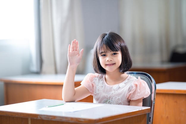 Eine asiatische Schülerin, die eine Hand hebt, um Lehrerfragen im Klassenzimmer zu stellen