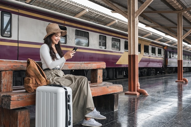 Eine asiatische Teenagerin benutzt ihr Smartphone, während sie an einem Bahnhof auf einen Zug wartet