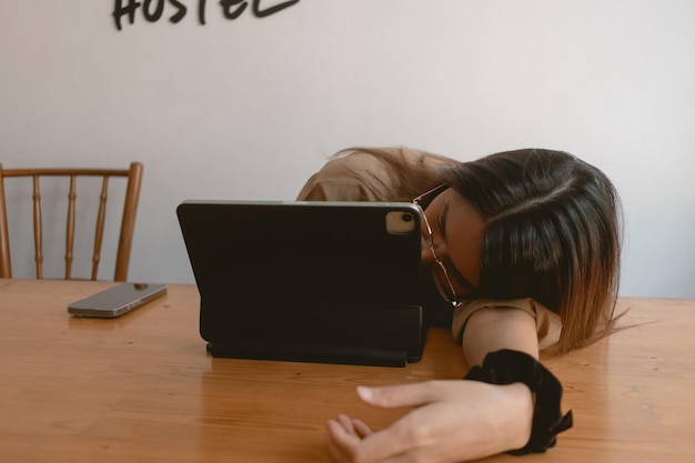 Eine asiatische thailändische Frau schläft ein, legt ihren Kopf auf den Arm und arbeitet und benutzt einen Laptop.