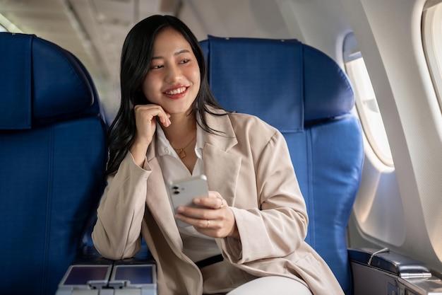 Eine attraktive asiatische Geschäftsfrau sitzt am Fenster mit einem Smartphone in der Hand