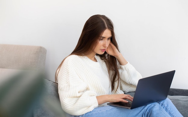 Eine attraktive Brünette sitzt zu Hause auf der Couch und nutzt einen Laptop für Online-Training