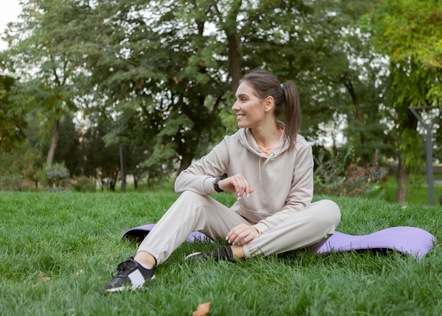 Eine attraktive fitte Frau ruht sich aus, während sie im Park auf der Matte sitzt Fitness oder Yoga im Freien