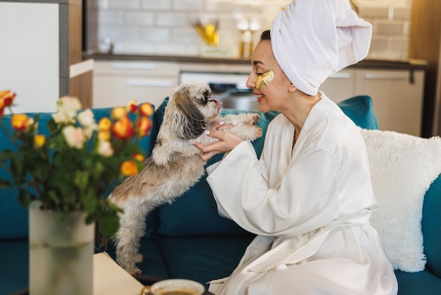 Eine attraktive Frau spielt und entspannt sich mit ihrem kleinen Shih Tzu-Hund, während sie den Morgen zu Hause genießt.