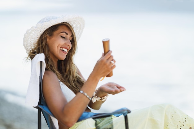 Eine attraktive junge Frau benutzt Sonnencreme und genießt die Zeit am Strand.