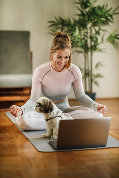 Eine attraktive junge Frau, die mit einem Laptop ihren Vlog über gesundes Leben aufzeichnet, während sie zu Hause Übungen macht.