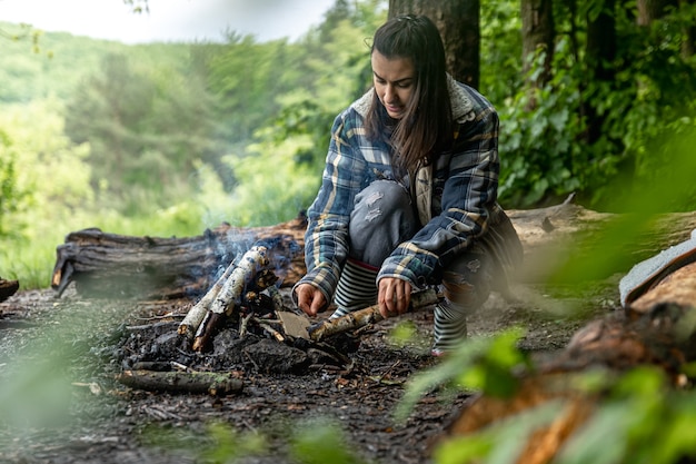 Eine attraktive junge Frau macht ein Feuer, um sich im Wald warm zu halten