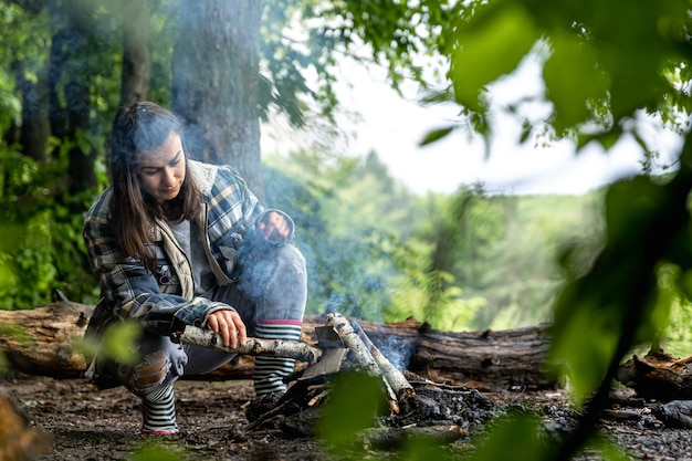 Eine attraktive junge Frau macht ein Feuer, um sich im Wald warm zu halten