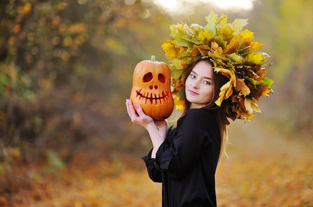 Eine attraktive junge frau mit einem kranz aus herbstblättern auf dem kopf hält jacks laterne in den händen