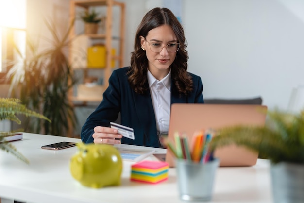 Eine attraktive junge Geschäftsfrau, die Zahlungen leistet, während sie an ihrem Computer im Büro arbeitet