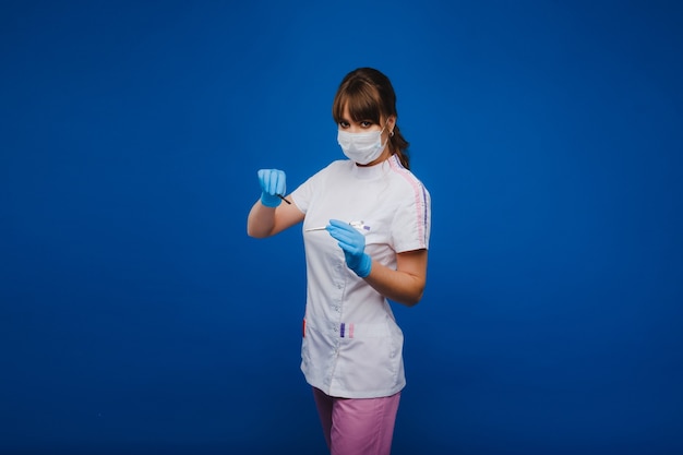 Eine attraktive junge Ärztin hält ein Skalpell und schaut direkt in die Kamera. Konzept der Gesundheitsversorgung, Behandlung und Chirurgie. Porträt eines Arztes auf blauem Hintergrund