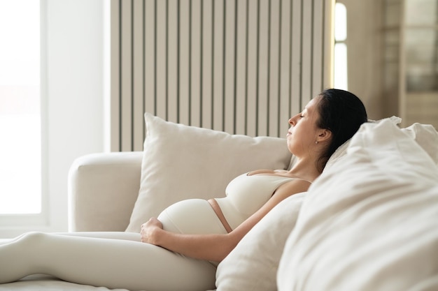 Eine attraktive schwangere Frau sitzt auf einem Sofa im Wohnzimmer ihres Hauses