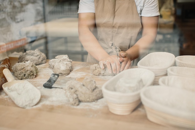 Eine Bäckerin knetet den Teig und legt ihn in eine Holzform Bäckereikonzept