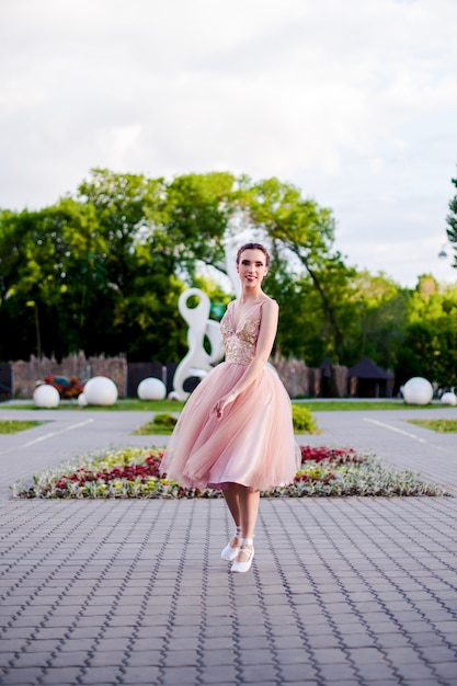 Eine Ballerina in einem langen rosa Seidenkleid dreht sich in einem Tanz im Park im Sommerballett im Stadtpark...